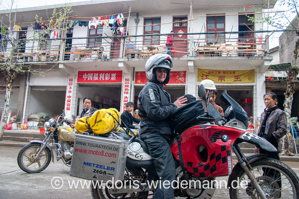 2006-China Doris Wiedemann sits in a rain suit on her Touratech conversion of a BMW F650GS Dakar in a small Chinese town